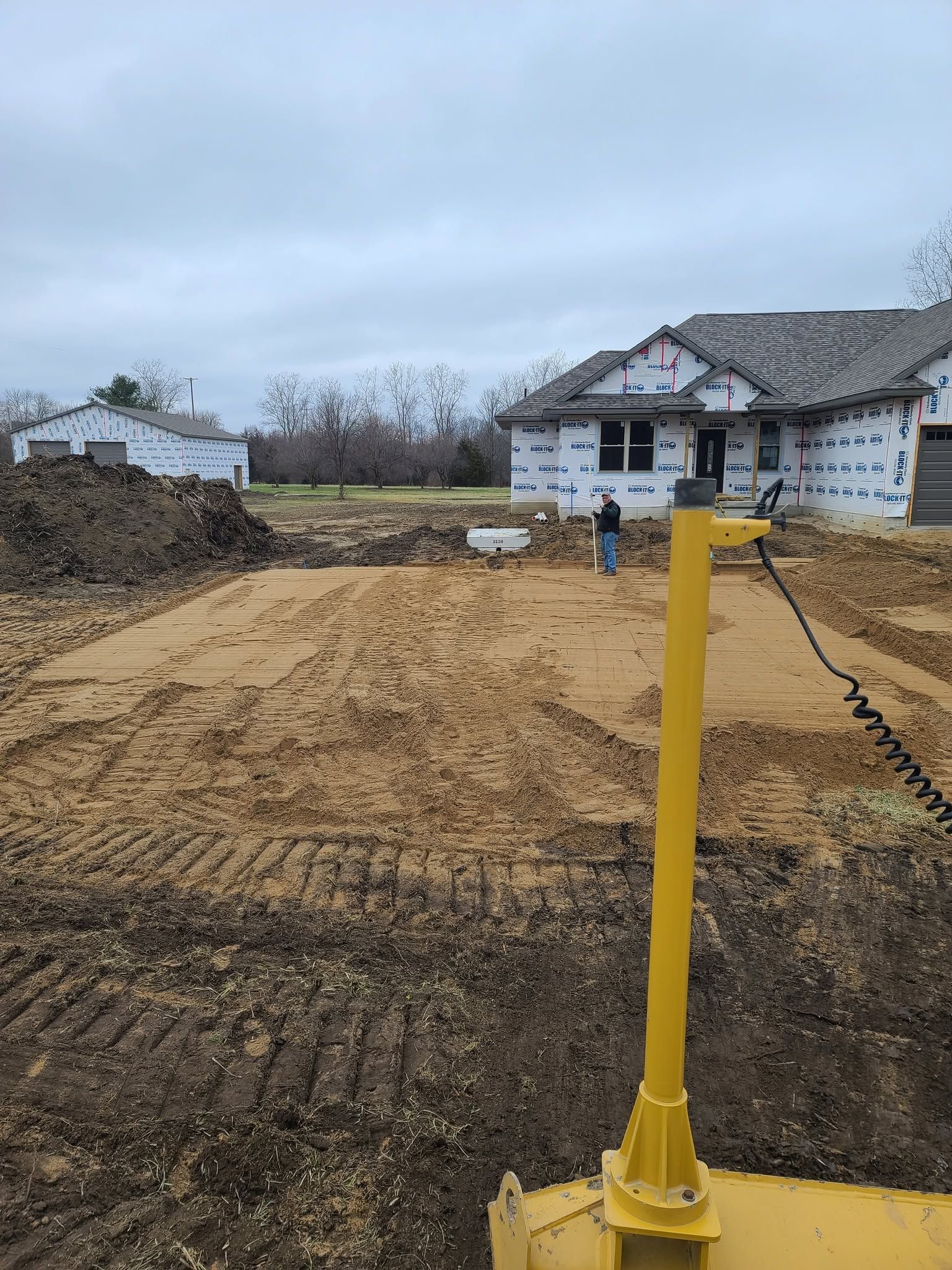 Construction site with a yellow survey stake in the foreground and a house under construction in the background.