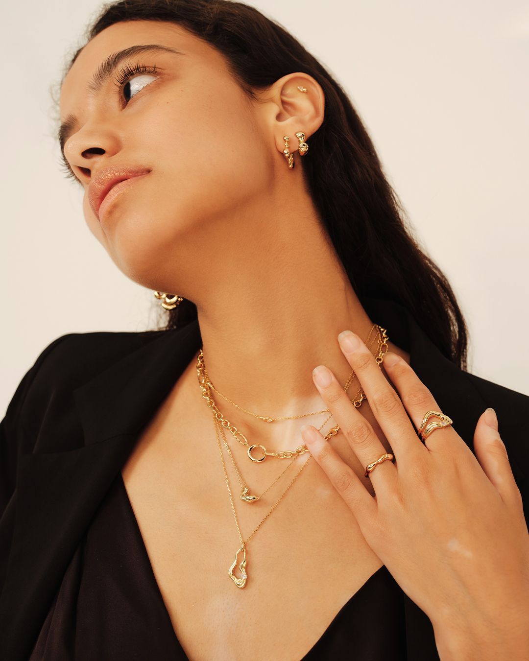 Femme portant des bijoux en or, notamment des boucles d'oreilles, des colliers et des bagues ; portrait en angle.