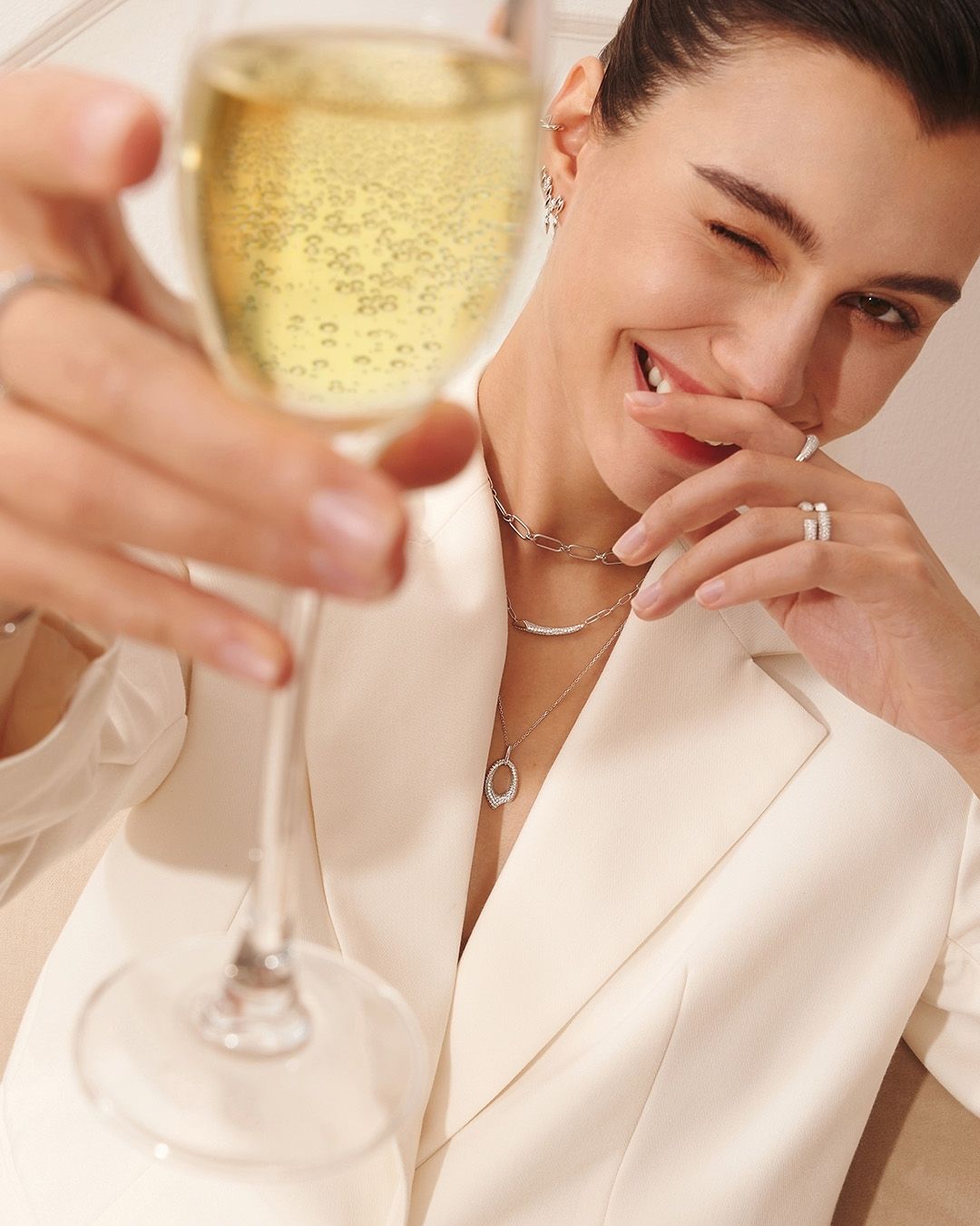Une femme en costume blanc fait un clin d'œil tout en tenant une flûte de champagne, célébrant.