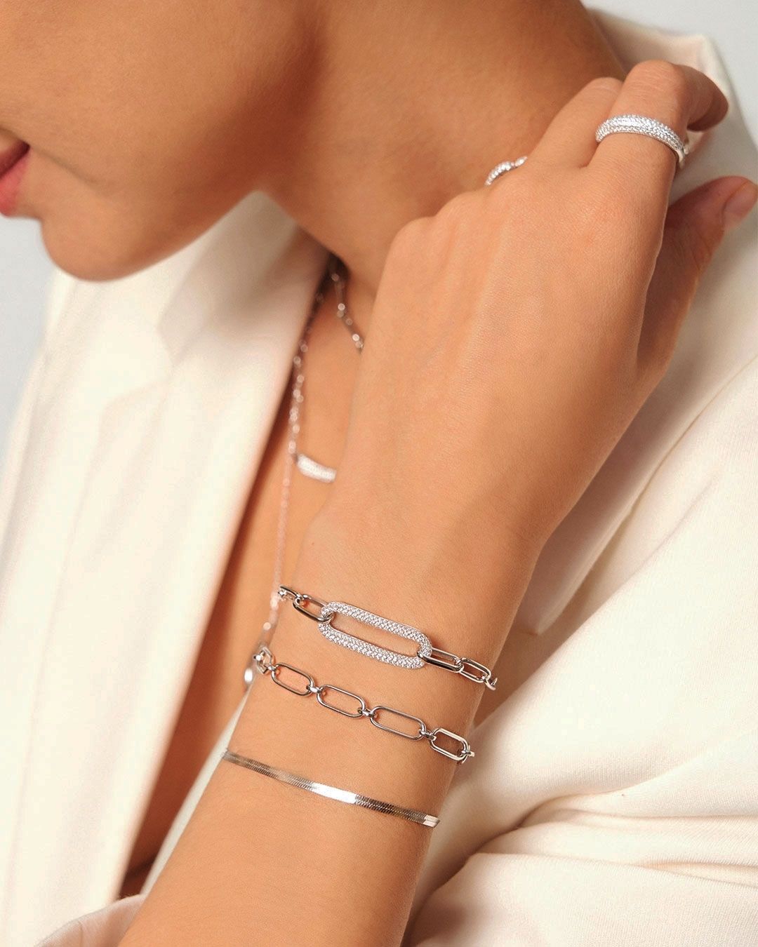 Bras d'une femme portant des bracelets et une bague en argent. Peau claire, vêtements neutres, main près de la bouche.