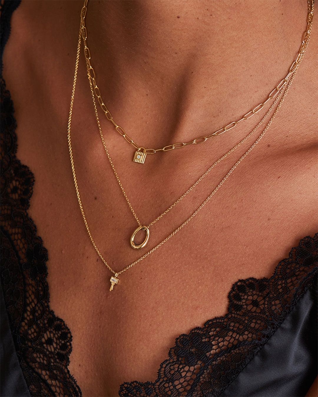 Gros plan de colliers en or superposés avec des pendentifs délicats sur le cou d'une femme, près d'une bordure en dentelle noire.