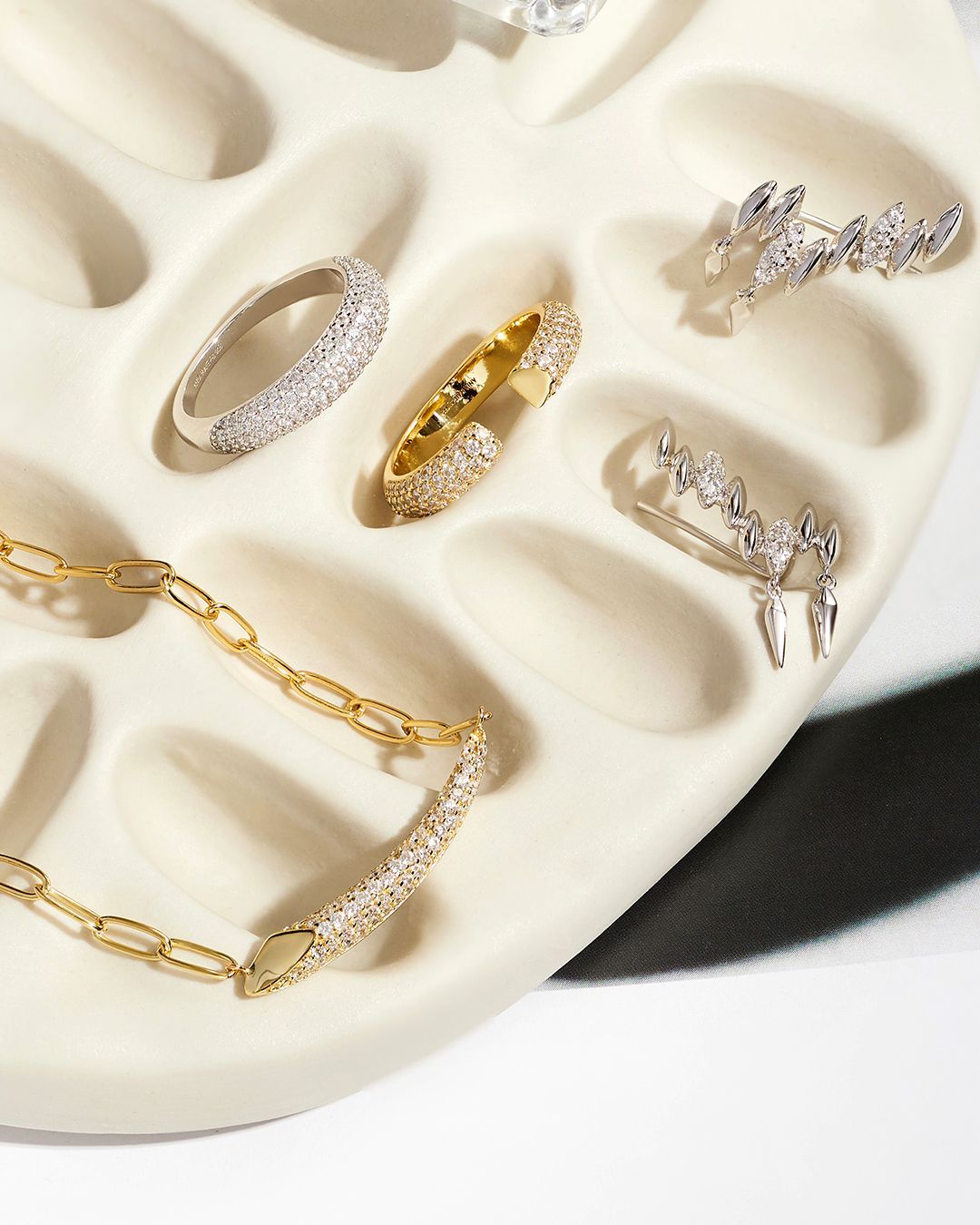 Bijoux présentés sur un plateau blanc texturé ; bagues, collier et boucles d'oreilles avec pierres précieuses.