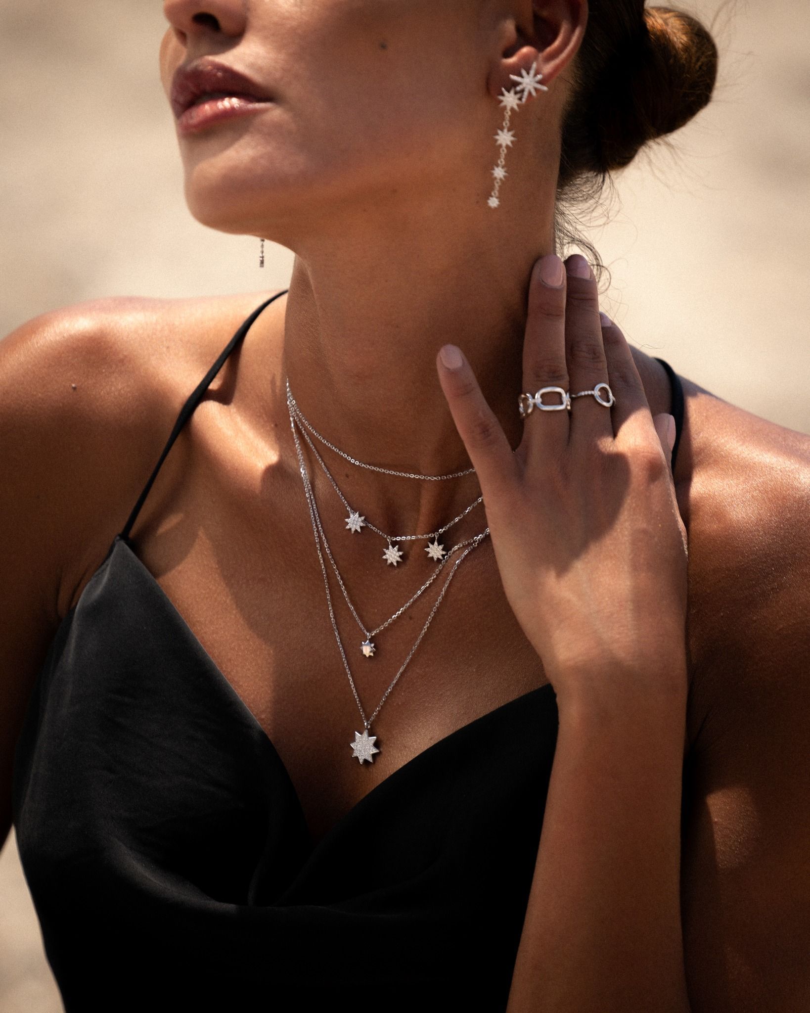 Femme portant des bijoux en forme d'étoile : boucles d'oreilles, colliers et une bague, avec une robe noire, en extérieur.