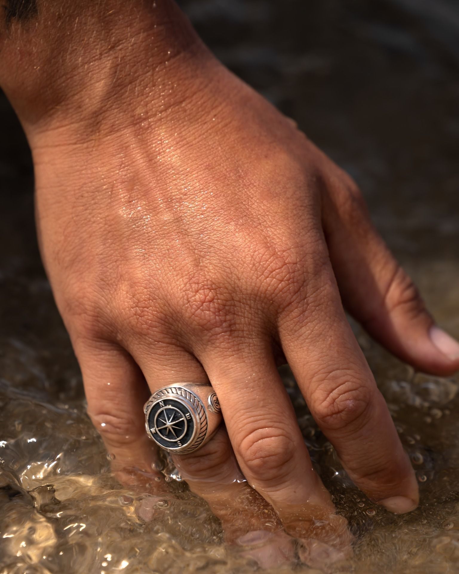Main avec un anneau de boussole dans l'eau peu profonde.