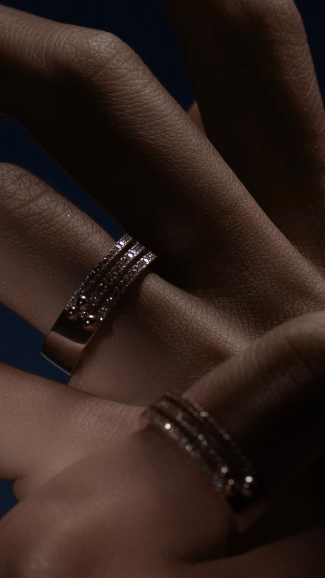 Gros plan de deux mains portant chacune une bague en diamant. Fond sombre.
