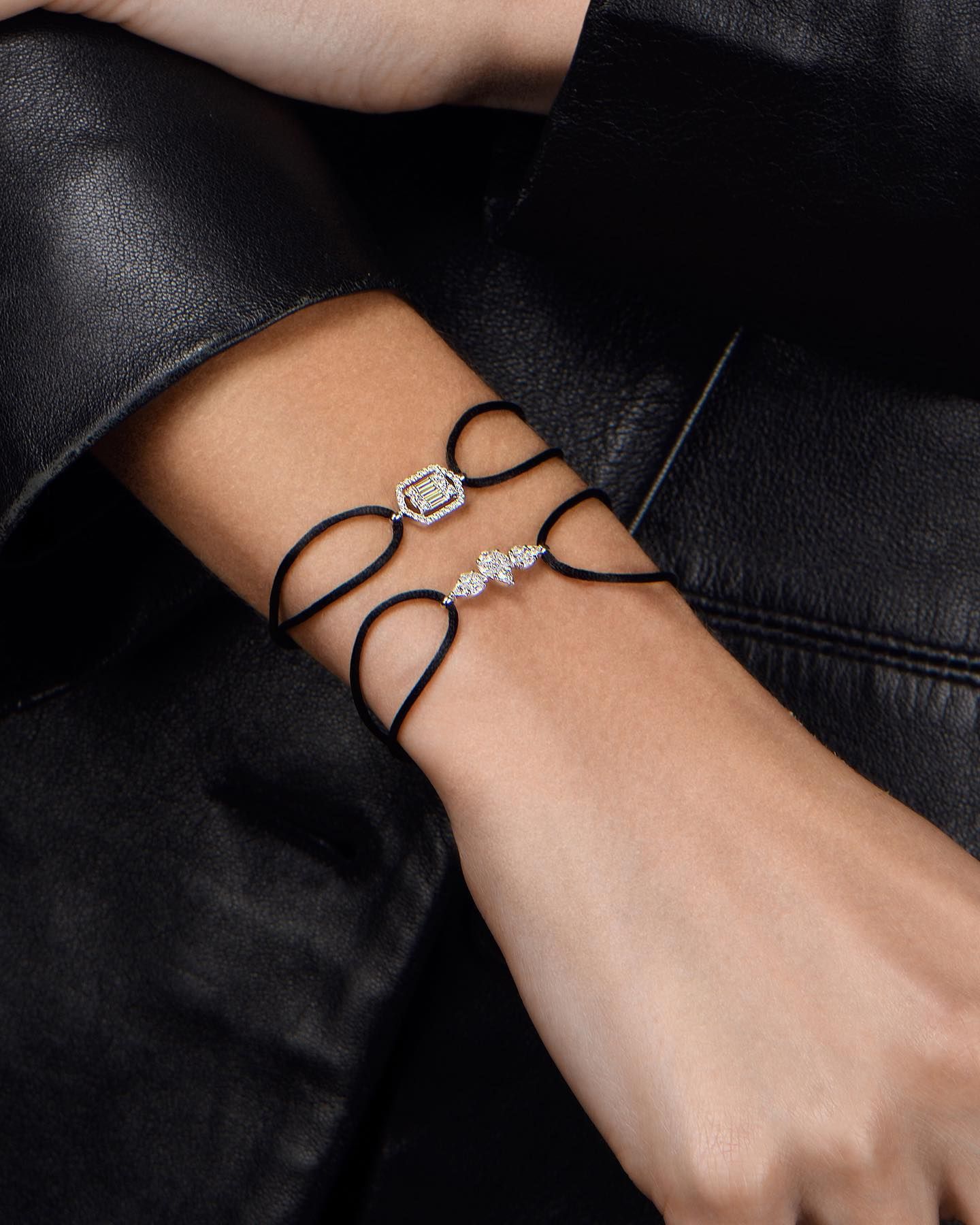 Deux bracelets en diamant sur un poignet avec une veste en cuir noir, un bracelet a une forme hexagonale et l'autre a trois pierres en diamant.