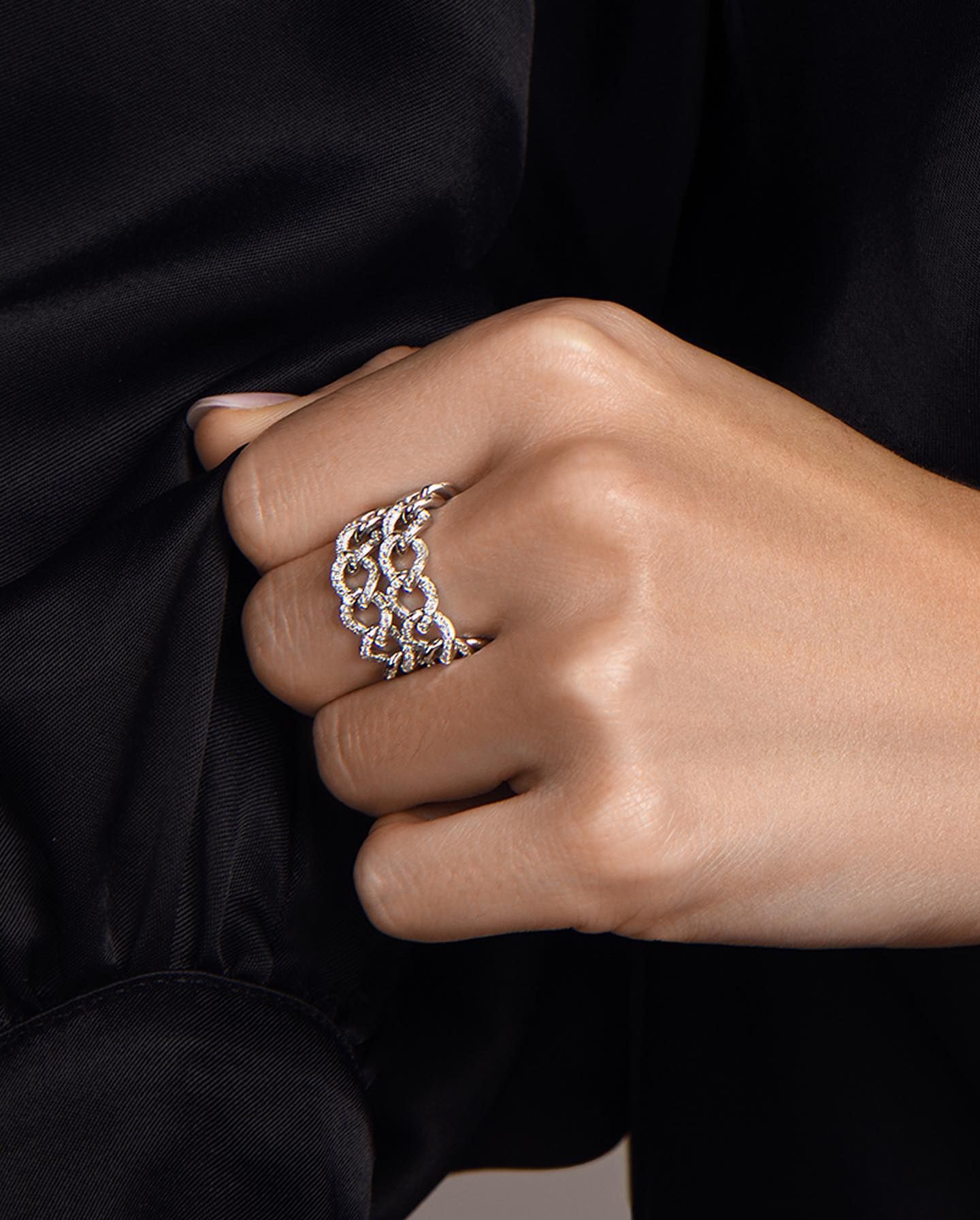 Main portant une bague à maillons en argent, posée contre un vêtement noir.