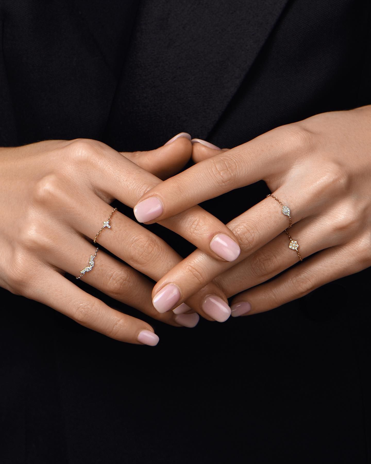 Mains portant de délicates bagues en diamant, sur fond noir.