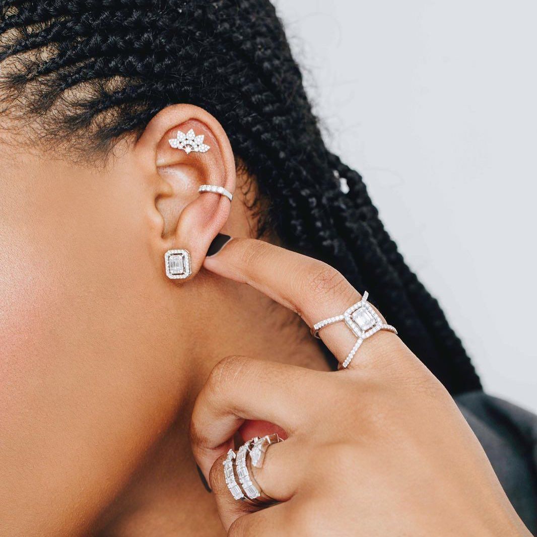 Femme aux cheveux tressés, portant des boucles d'oreilles en diamant, une manchette d'oreille et des bagues, touchant son oreille.