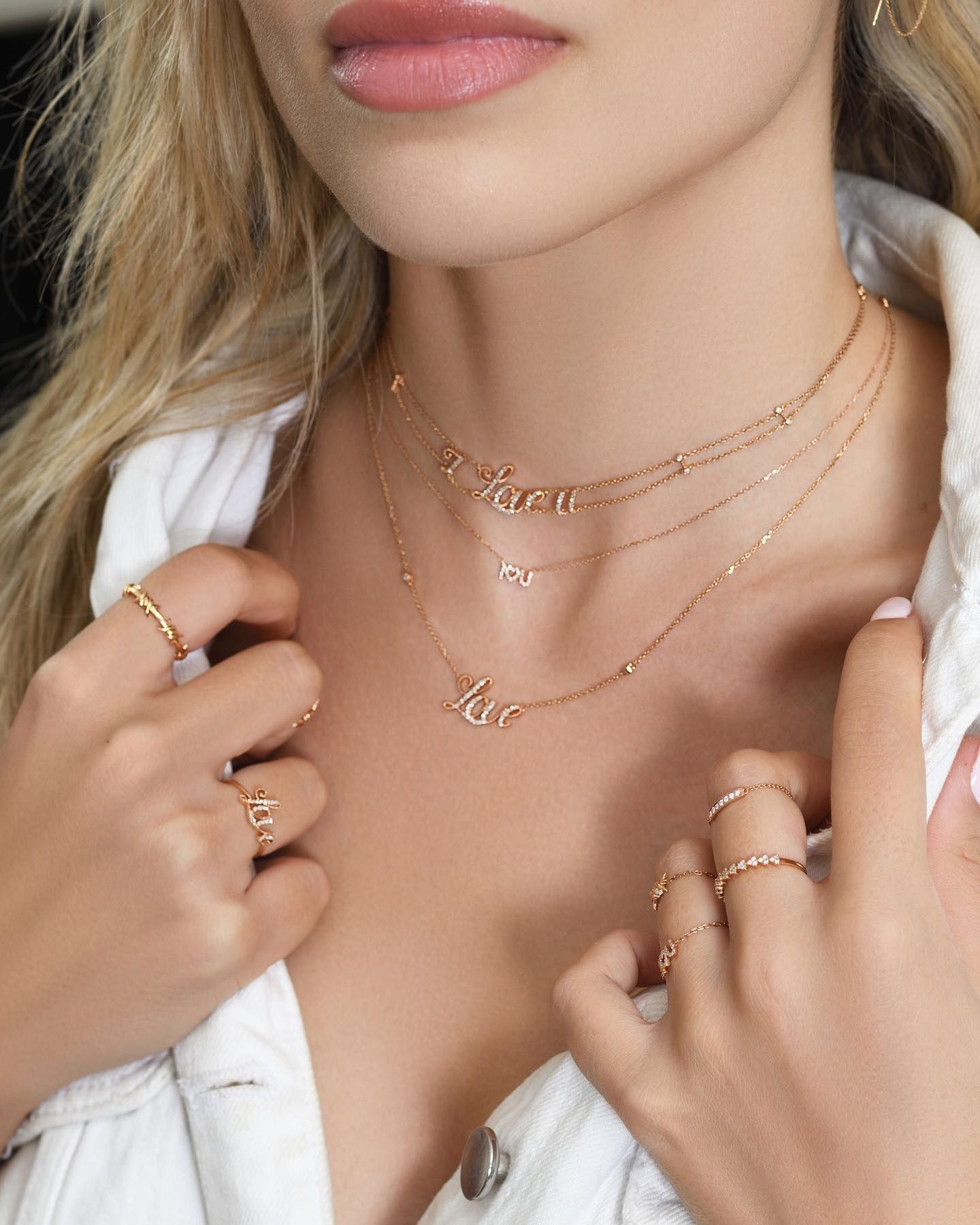 Femme portant des colliers et des bagues en or ; pendentifs « amour » et « pour toujours » ; veste en jean blanche.