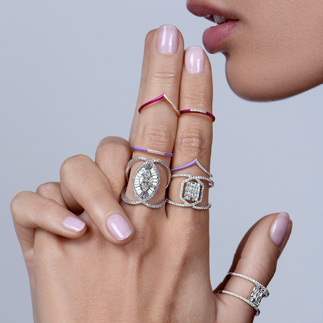 Main de femme aux multiples bagues, doigt sur les lèvres, laissant deviner le silence. Ongles rose pâle.