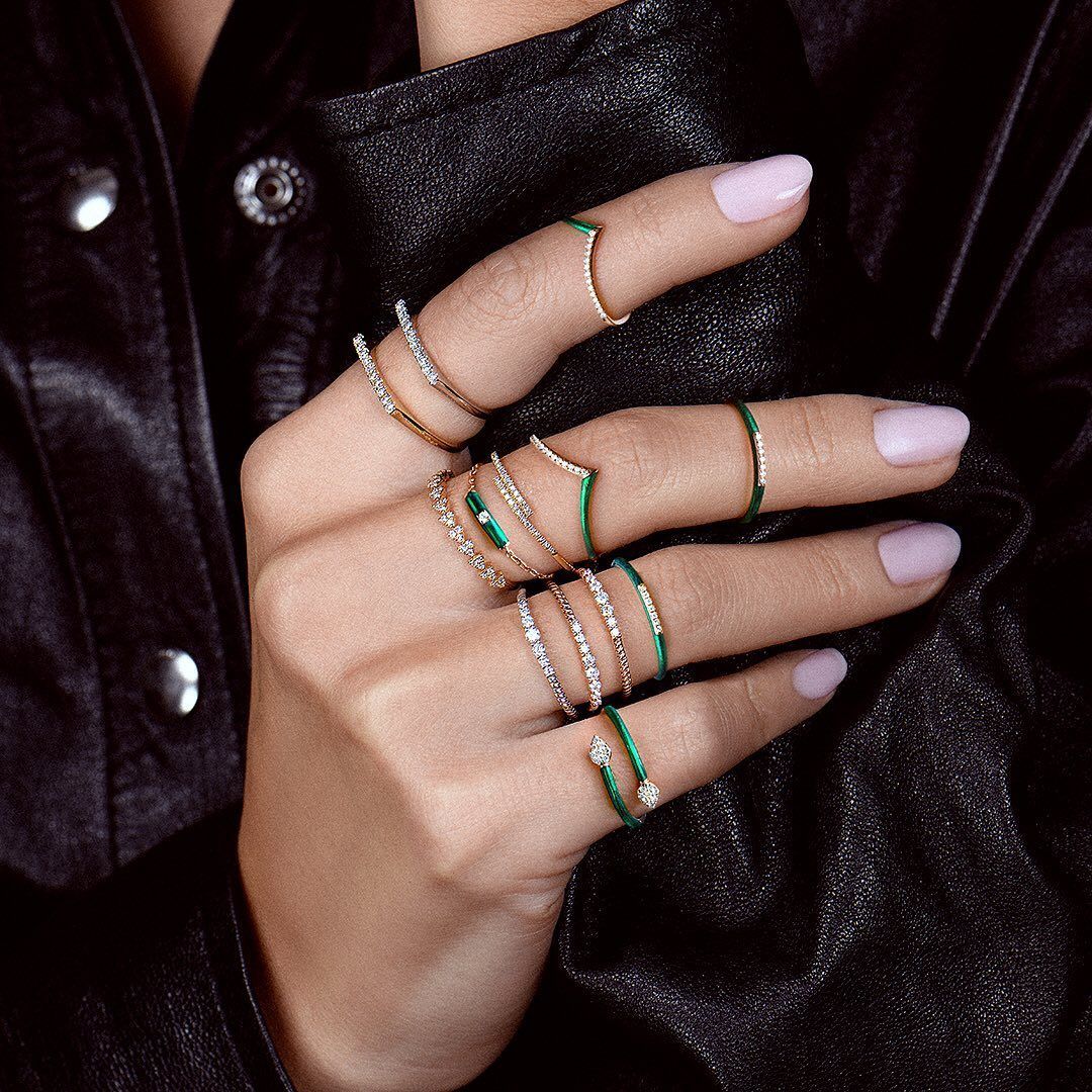 Main avec plusieurs bagues, certaines avec émail vert, sur fond de veste en cuir noir.