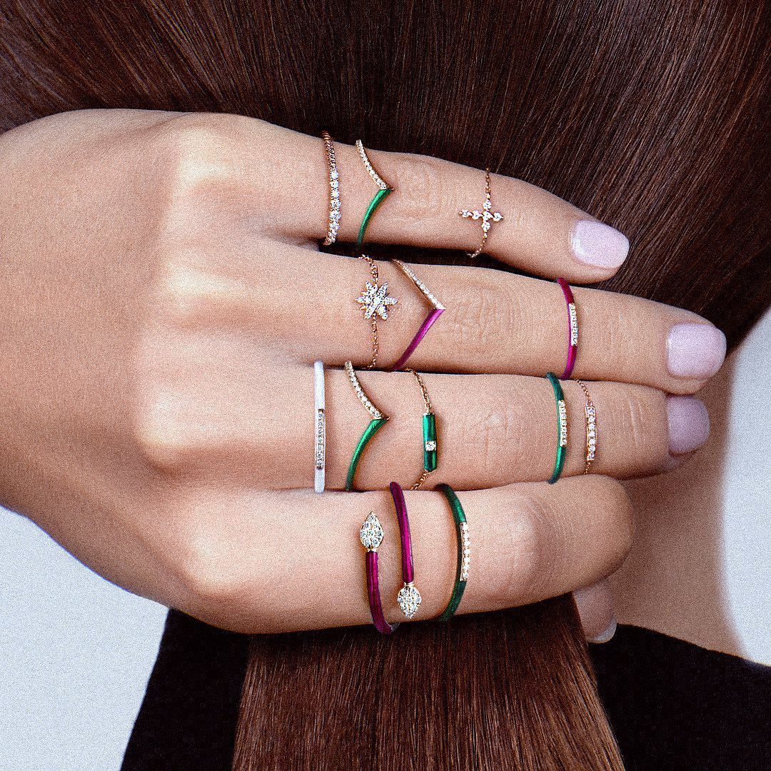 Main avec de nombreux anneaux, y compris des bandes aux tons de bijoux en or, verts et roses.