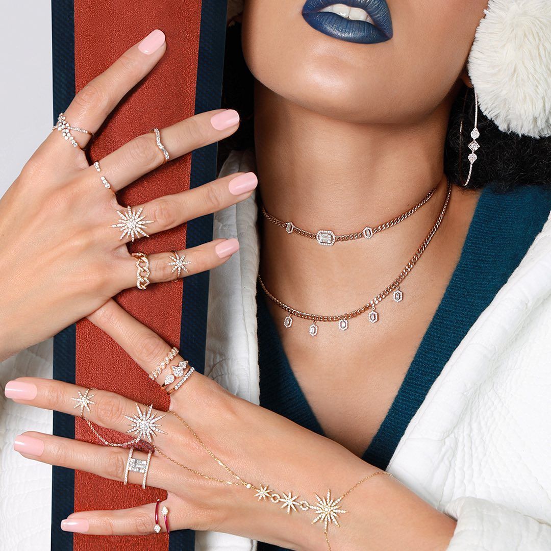 Femme portant plusieurs bagues, colliers et boucles d'oreilles. Rouge à lèvres bleu, veste rayée rouge et blanche.