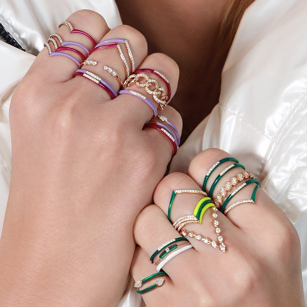 Mains avec plusieurs anneaux colorés, notamment en émail doré, rouge et vert et des accents de diamant.