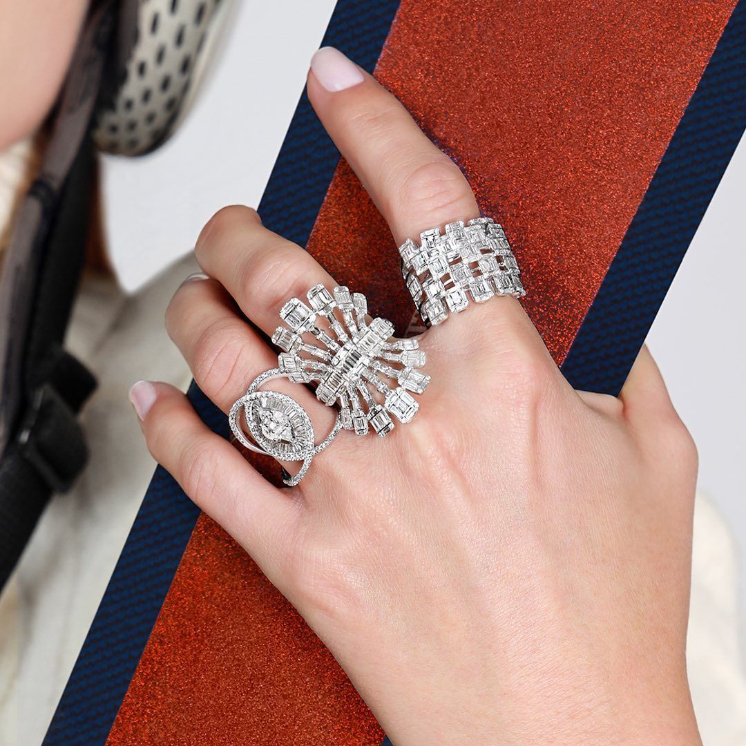 Main avec plusieurs bagues en diamant tenant un ski sur un fond neutre.