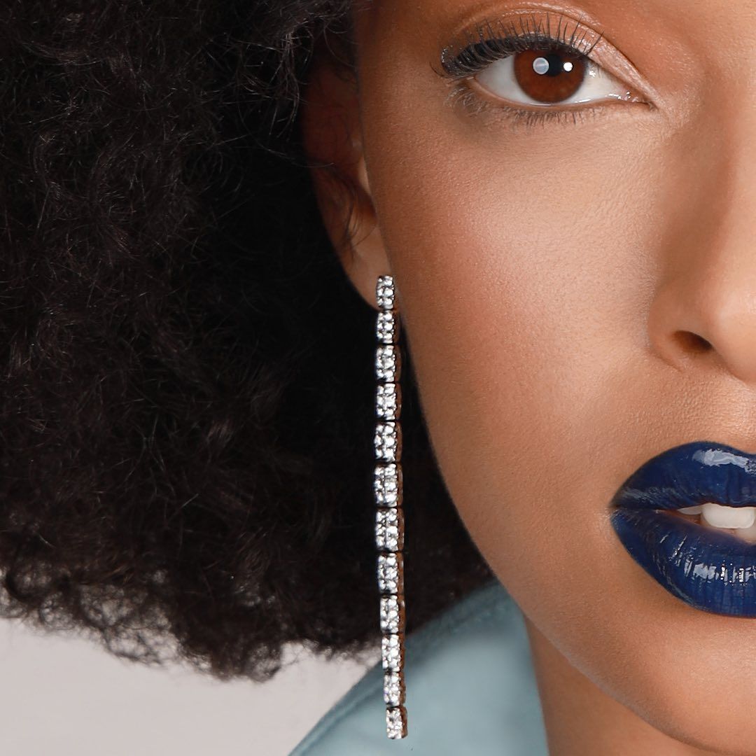 Gros plan d'une femme noire avec du rouge à lèvres bleu foncé et une boucle d'oreille en chaîne de diamant.