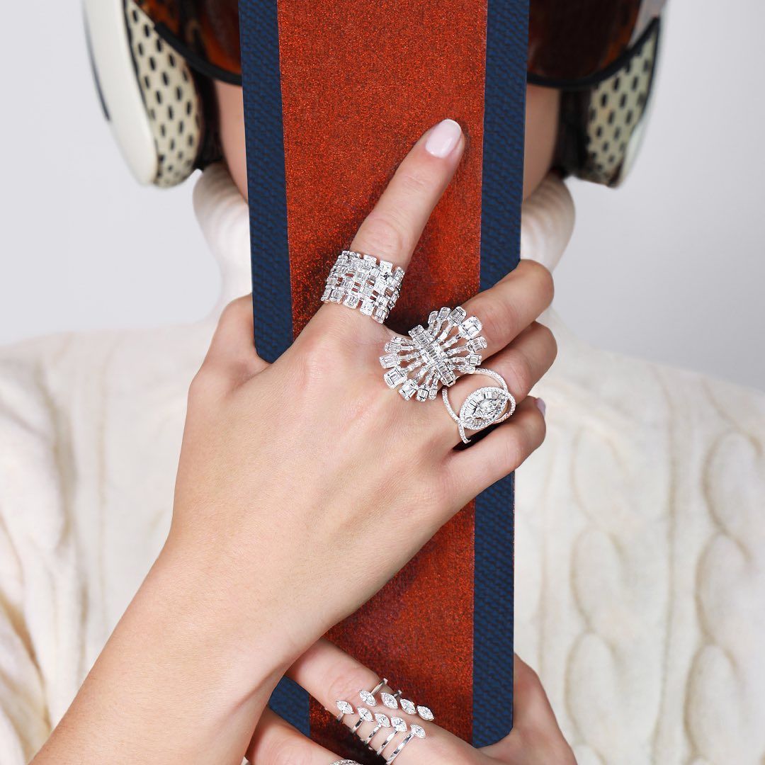 Femme portant un casque de ski et un pull, tenant un objet marron et bleu et portant plusieurs bagues en diamant.