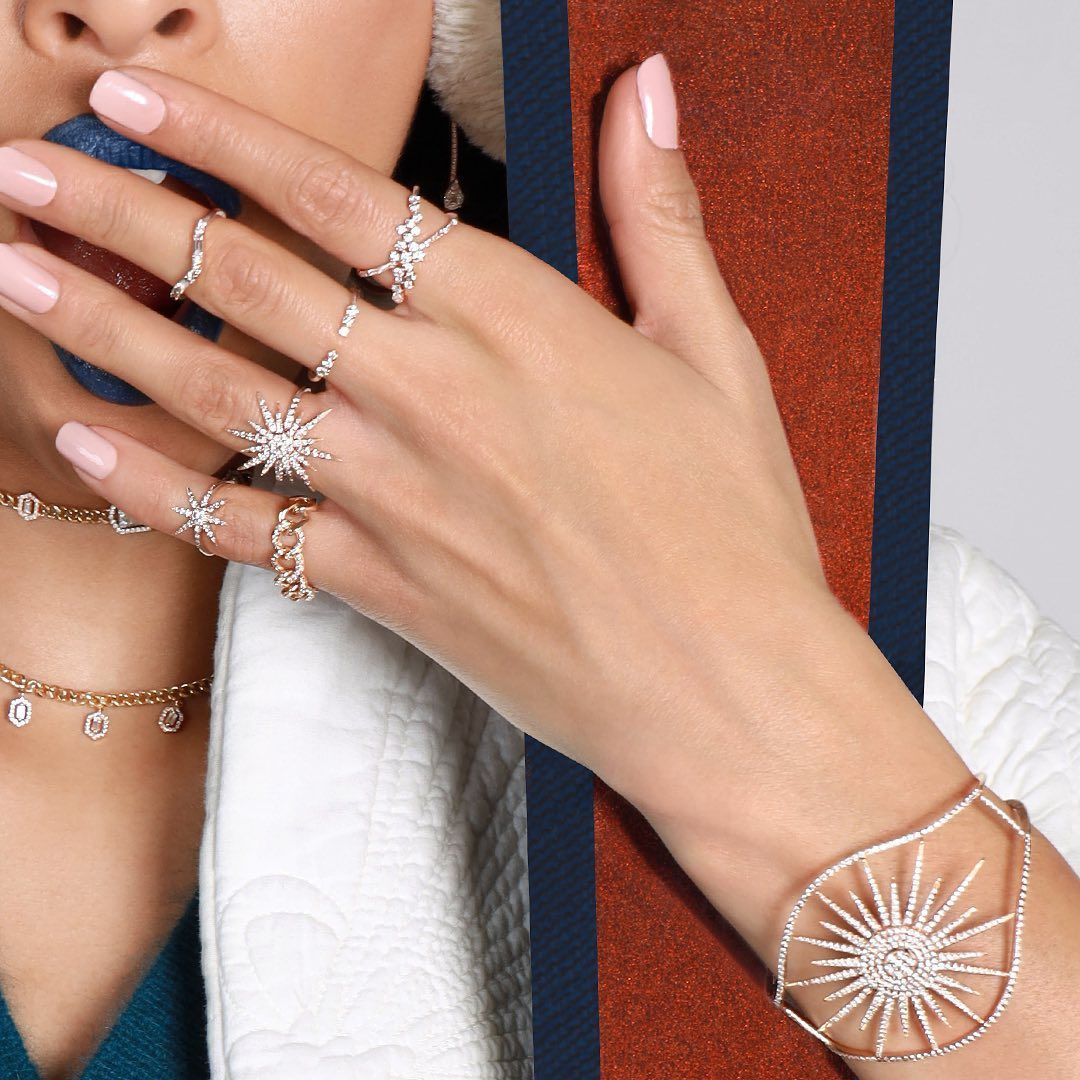 Main de femme avec bagues et bracelet scintillants. Ongles rose pâle. Tenant un tissu à rayures rouges et bleues.