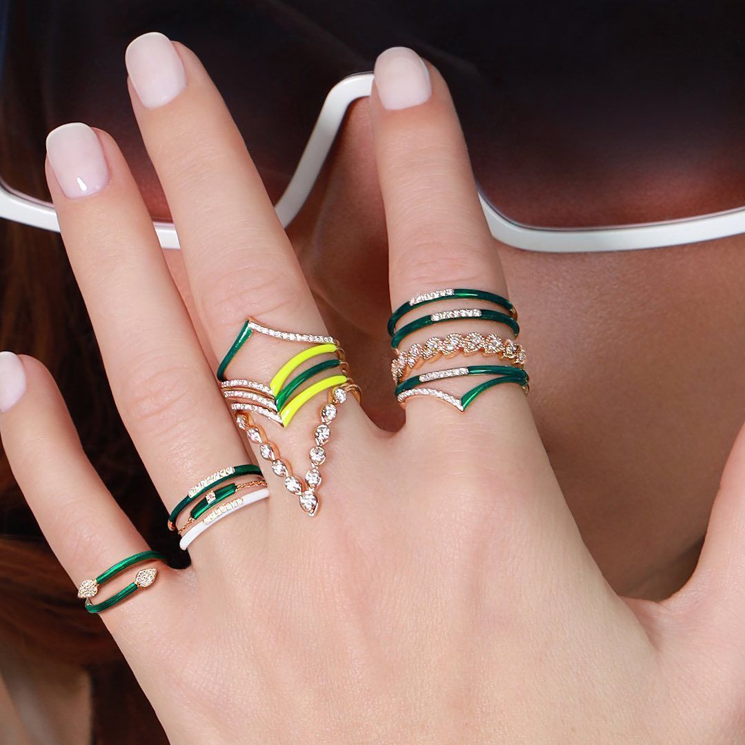 Main avec plusieurs anneaux : émail vert et jaune, diamants et lunettes de soleil blanches.