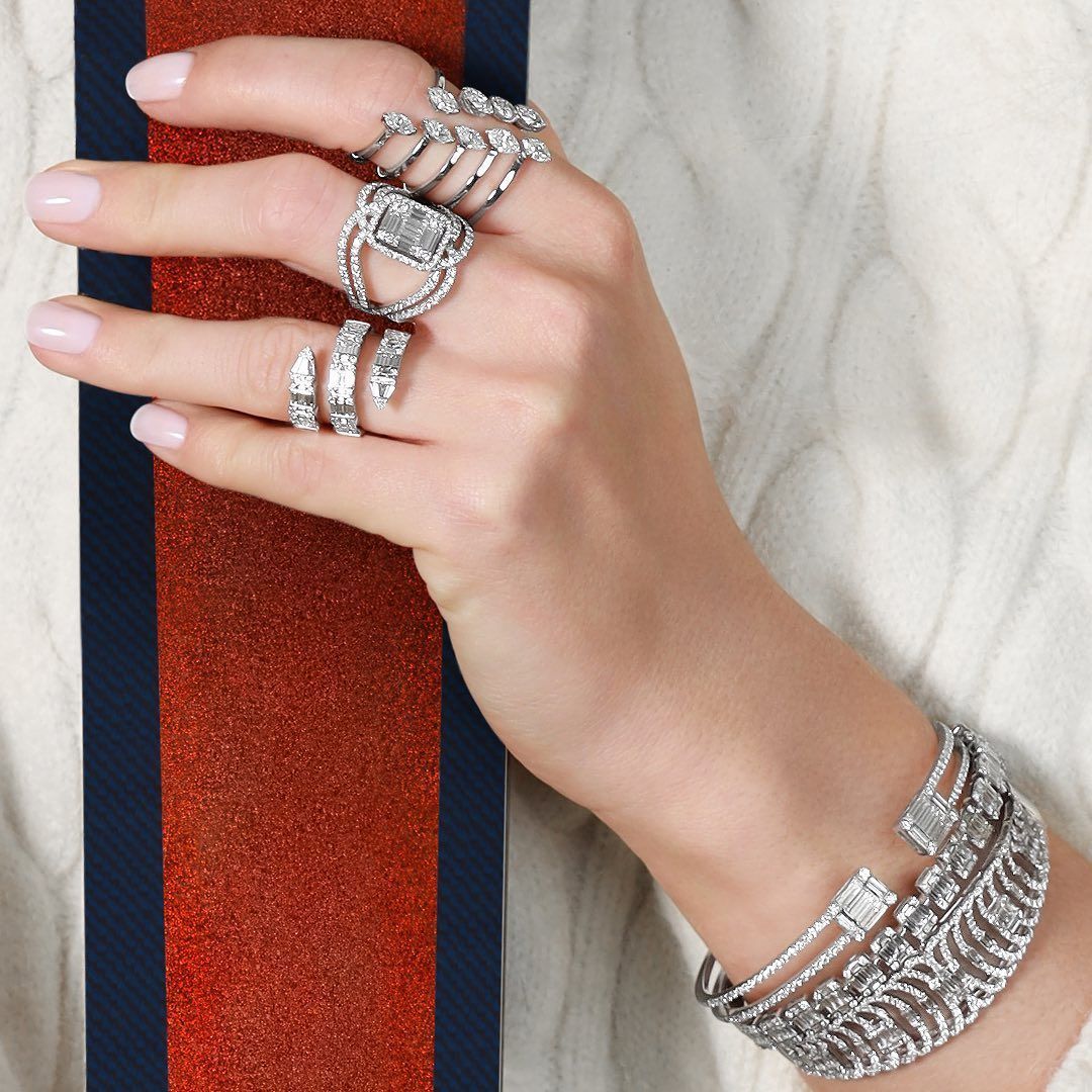 Main avec bagues et bracelet en diamant, portant un pull blanc à rayures rouges et bleu marine.