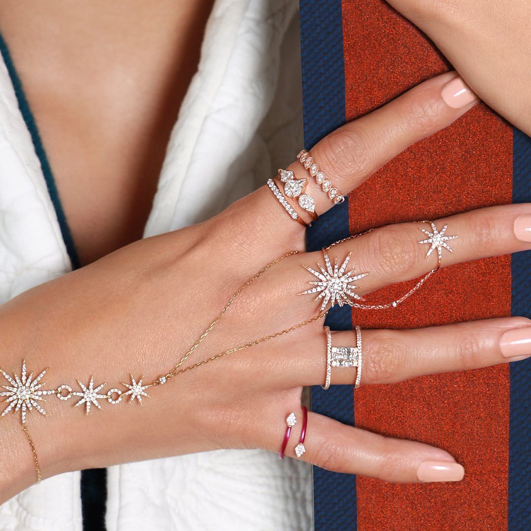 Main portant plusieurs bagues en diamant et une chaîne de main en forme d'étoile, reposant sur une surface rayée rouge et bleue.