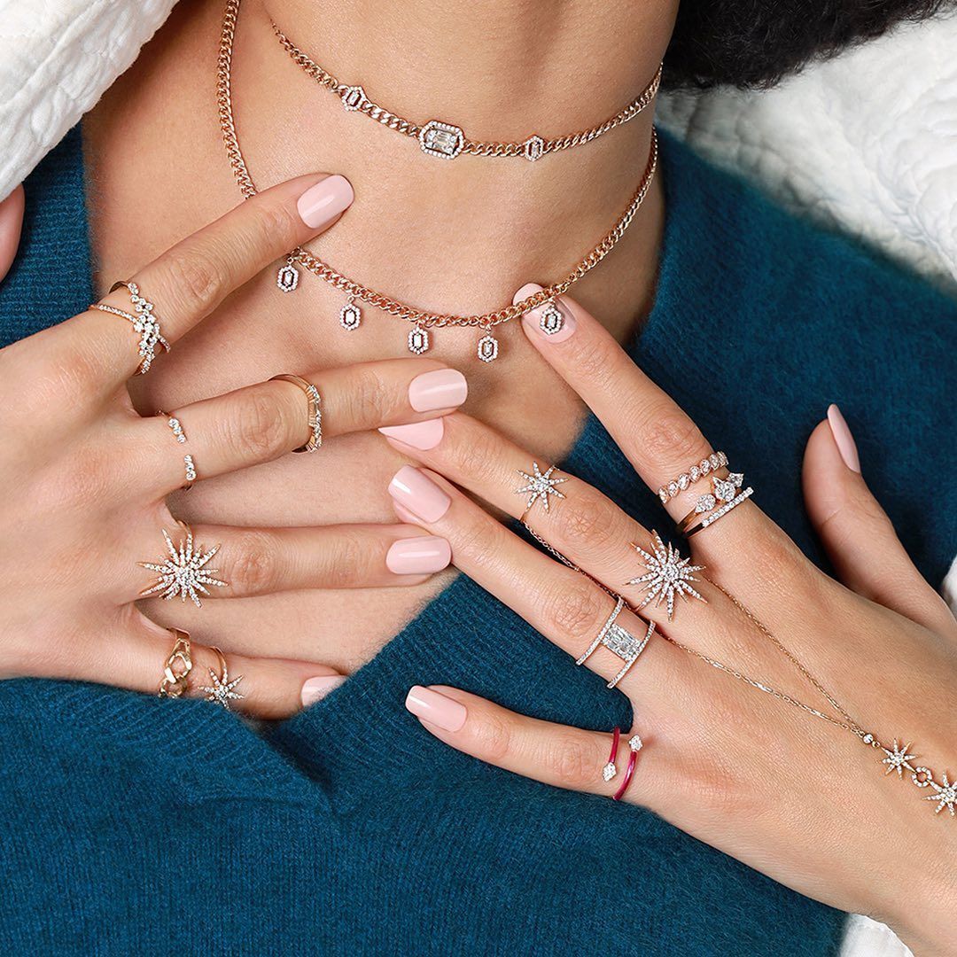 Mains de femme ornées de bagues et d'un collier avec des breloques pendantes, sur un dessus bleu sarcelle.