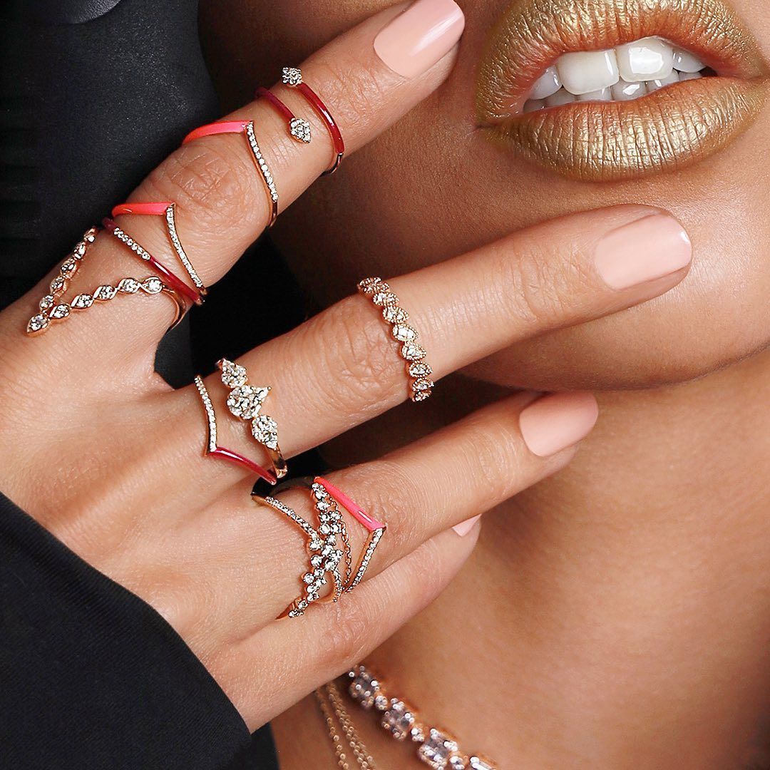 Main avec plusieurs anneaux, rouge à lèvres doré et ongles peints.