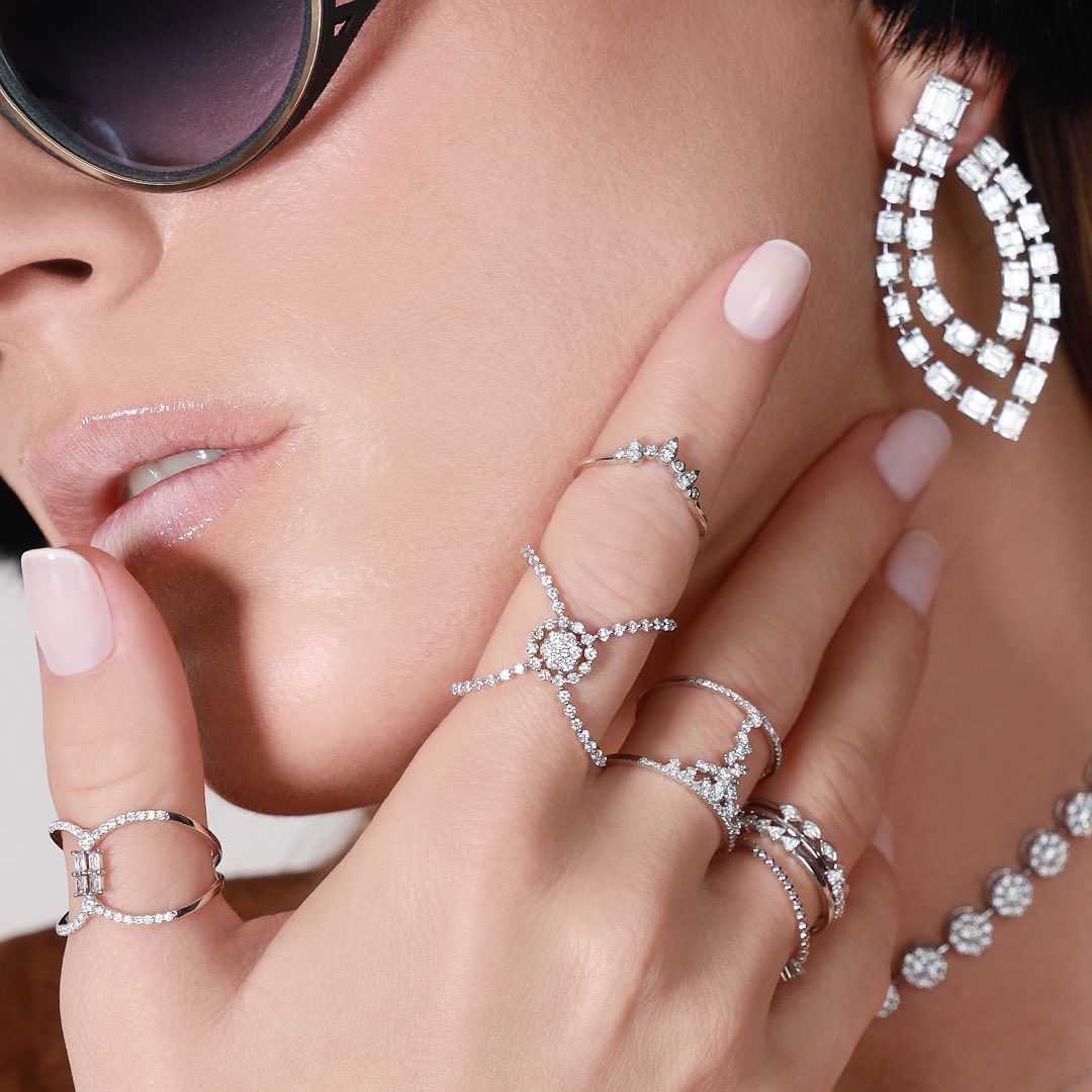 Femme avec plusieurs bagues et boucles d'oreilles en diamant, lunettes de soleil et collier.