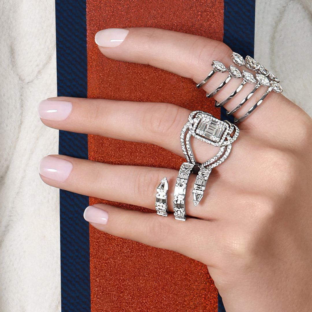 Main présentant plusieurs bagues en diamant, sur un fond blanc et rayé.