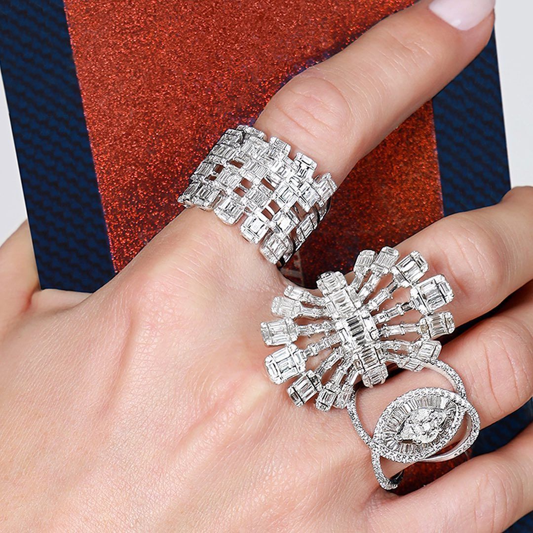 Main portant trois bagues en diamant élaborées, avec un fond rouge et bleu.