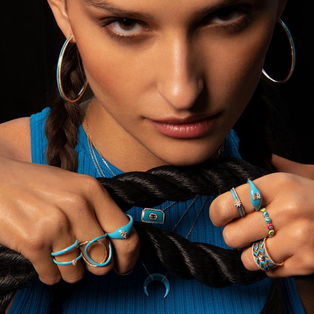Femme avec des tresses portant des bijoux turquoise, tenant une corde noire ; expression concentrée.