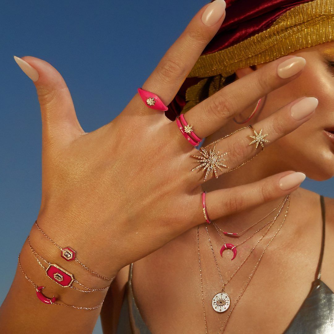 Main de femme ornée de bijoux roses et dorés, se détachant sur un ciel bleu.