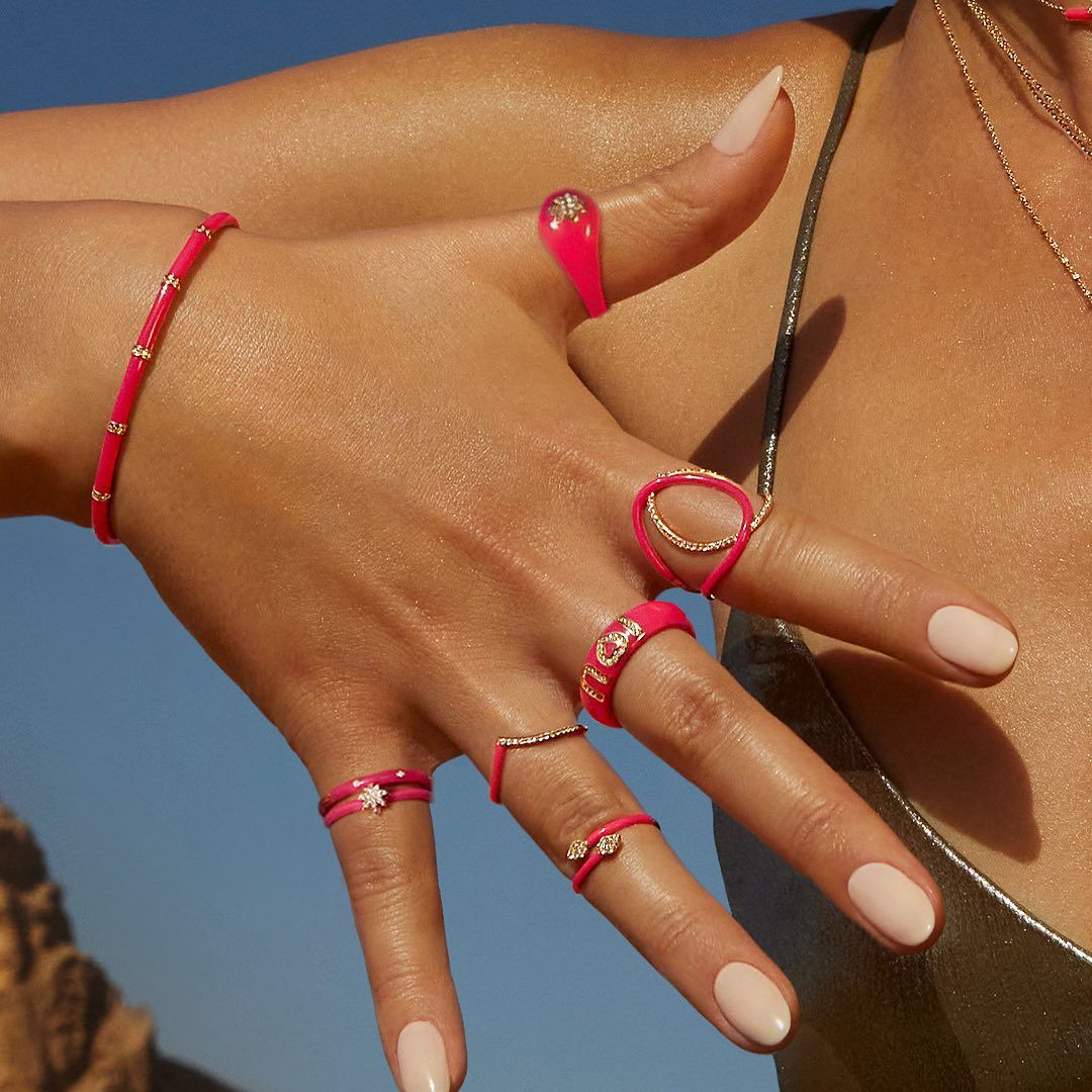 Main portant des bijoux roses avec des ongles manucurés, fond bleu.