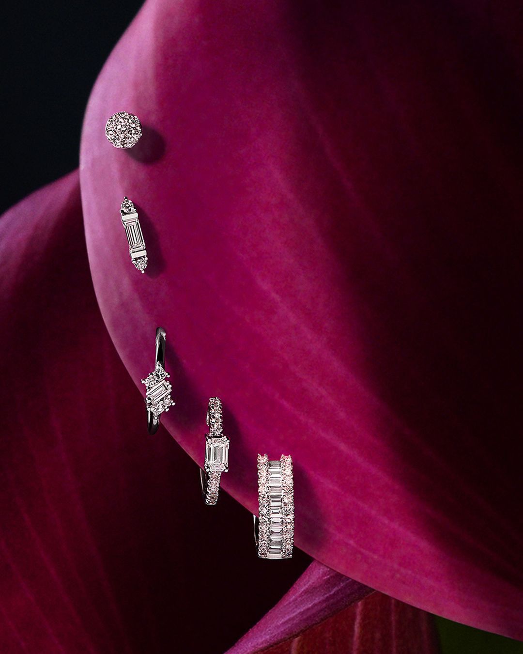 Boucles d'oreilles en diamant présentées sur un grand pétale de fleur rose foncé sur un fond sombre.