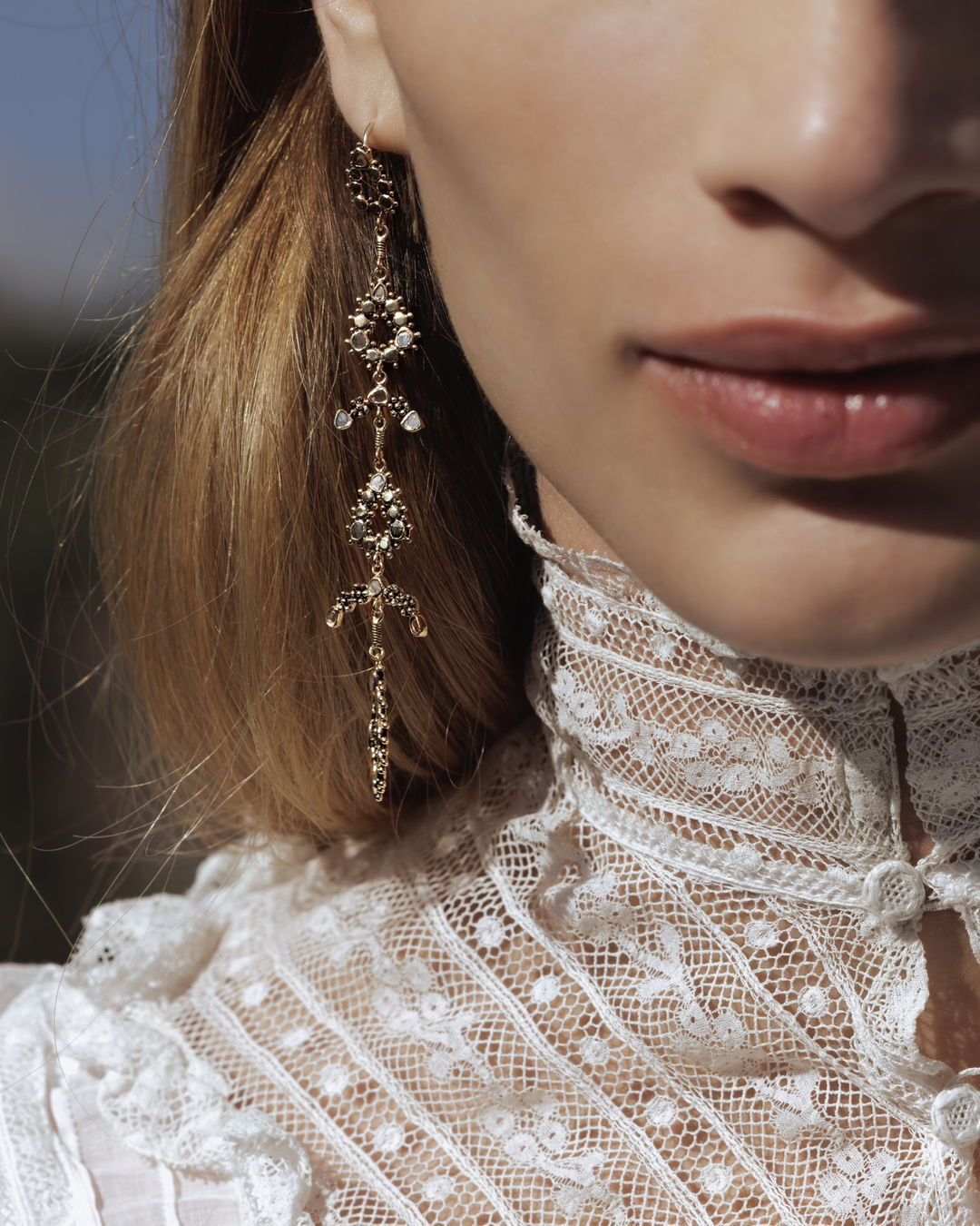 Femme portant de longues boucles d'oreilles en or, haut en dentelle blanche.