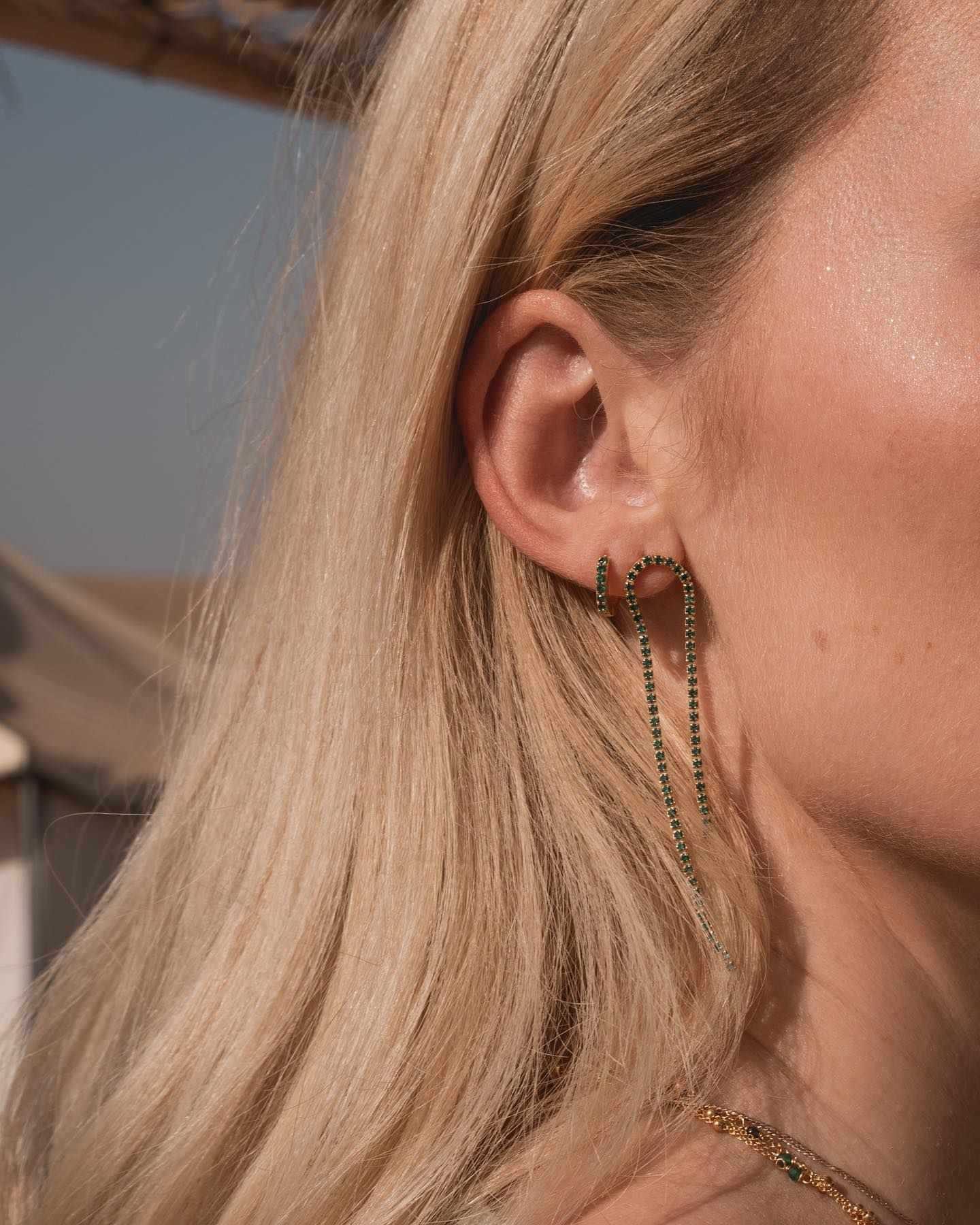 Oreille de femme avec boucles d'oreilles en pierres précieuses vertes, cheveux blonds, extérieur.
