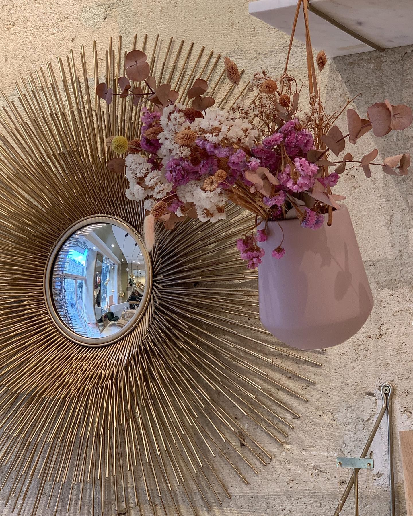 Miroir étoile doré et jardinière rose suspendue avec fleurs séchées contre un mur texturé.