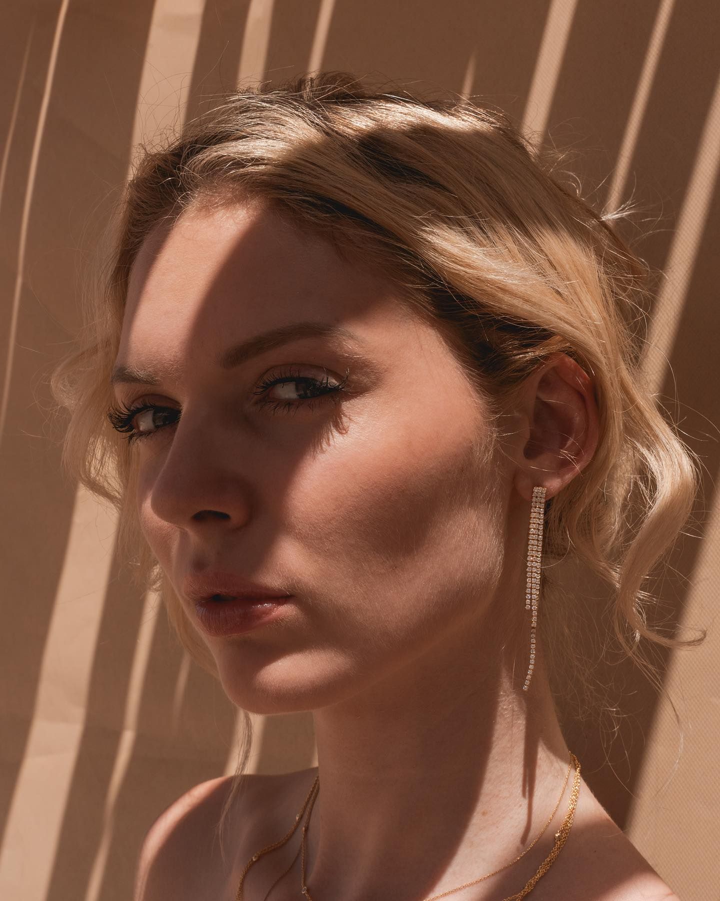 Femme aux cheveux blonds, portant des boucles d'oreilles, éclairée par des ombres.