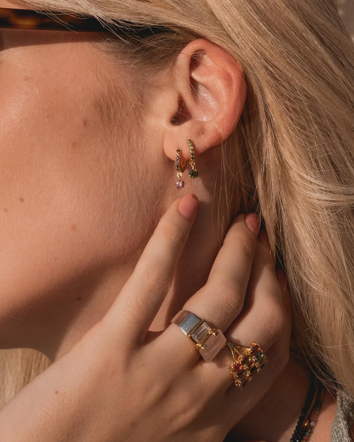 Oreille de femme avec créoles en or, main avec anneaux en or. Elle touche son oreille avec sa main.