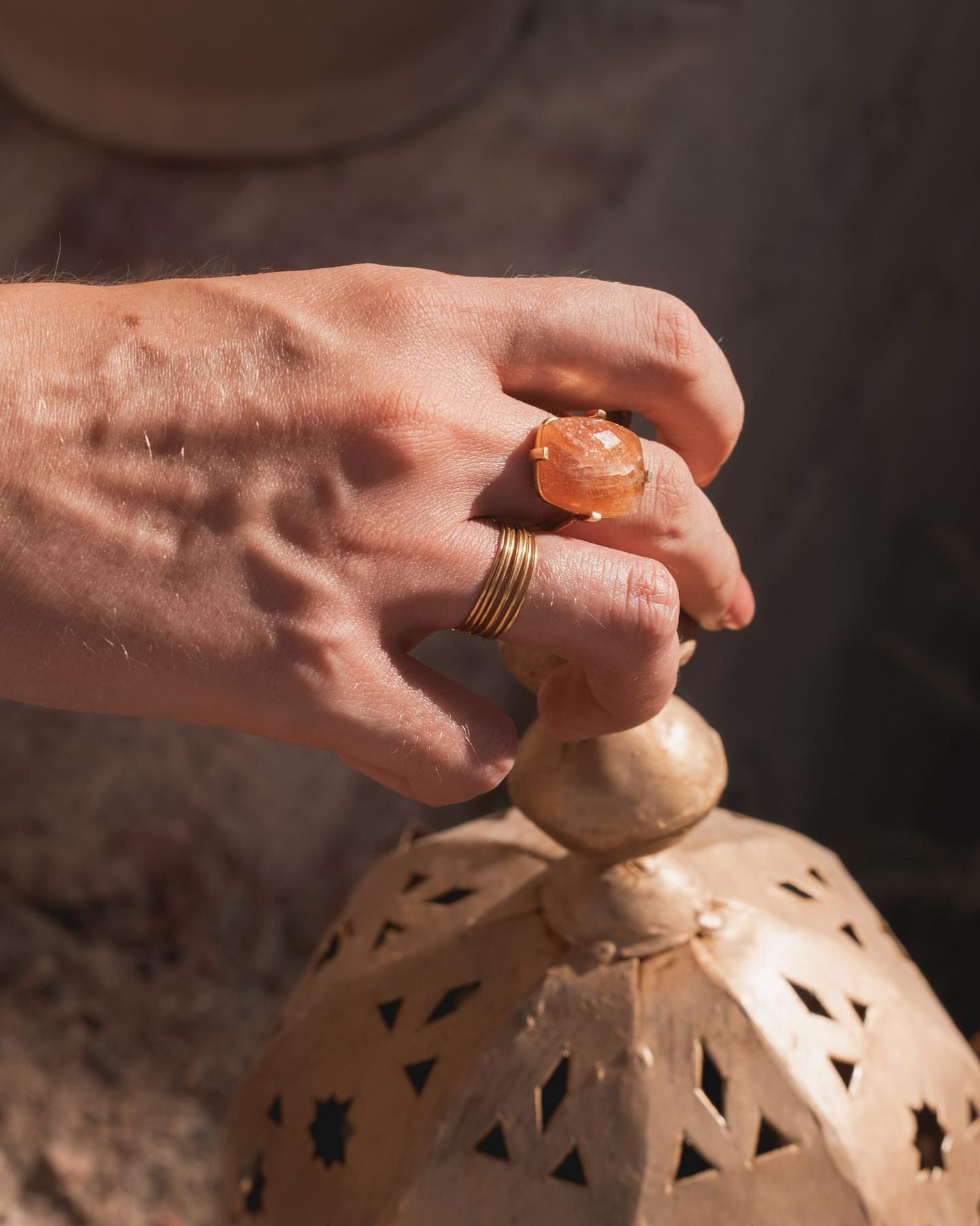 Une main portant des bagues tient une lanterne décorative en or.