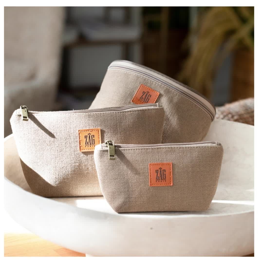 Trois sacs en toile beige avec fermeture éclair sur fond blanc. Chacun est muni d'une étiquette en cuir.