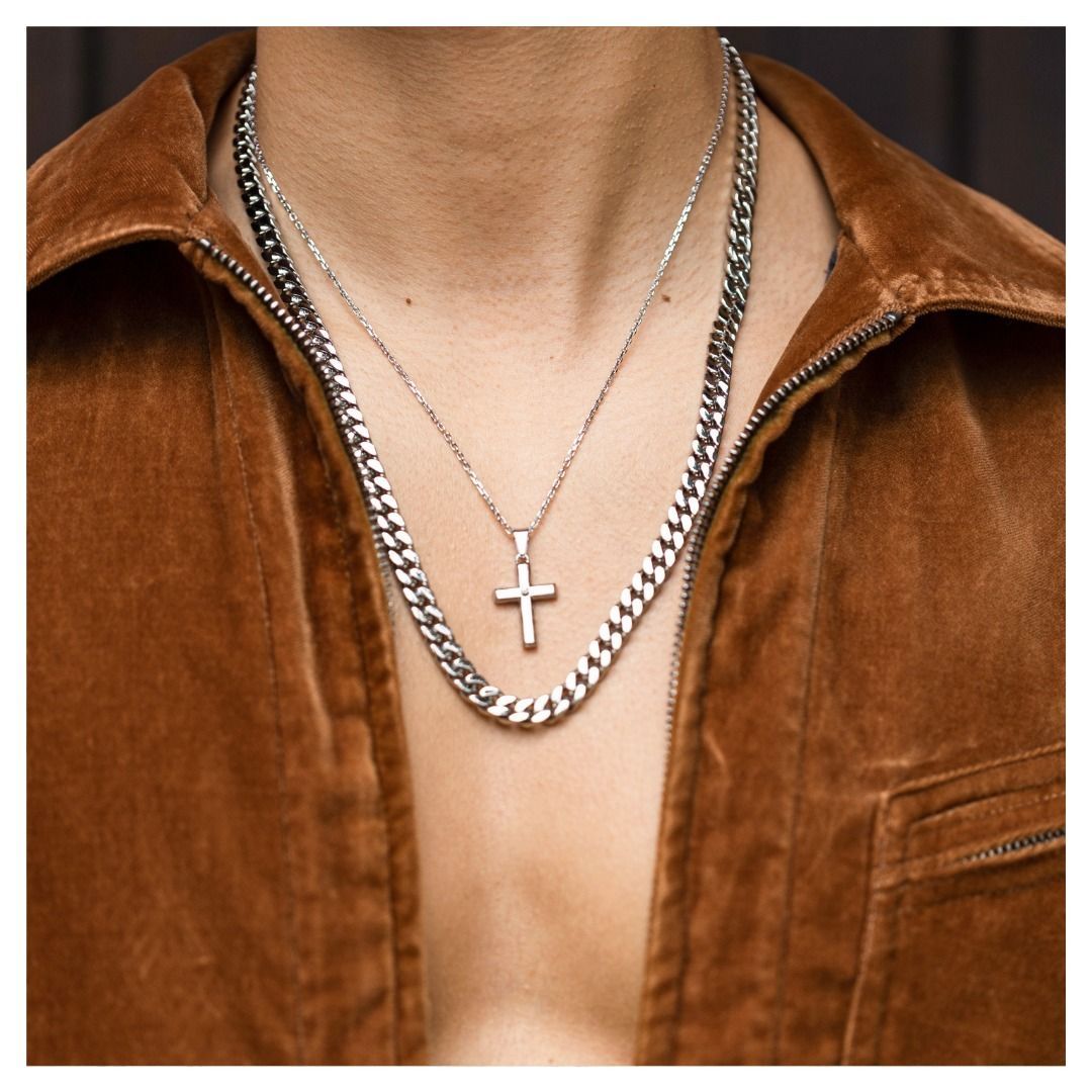 Homme portant une veste marron et deux colliers en argent, dont un avec un pendentif en forme de croix.