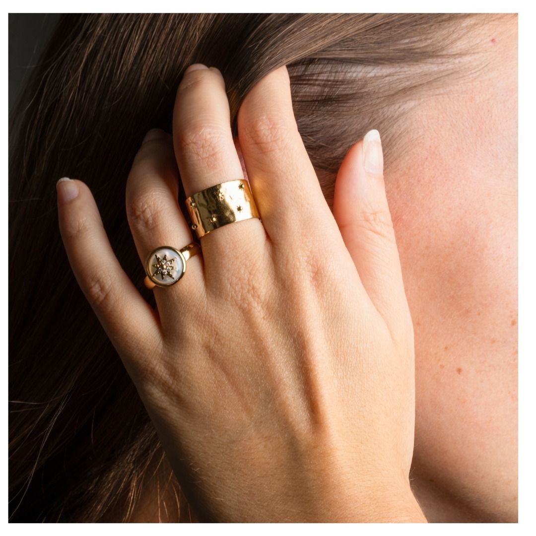 Main portant des bagues en or, touchant les cheveux, éclairée par la lumière du soleil.