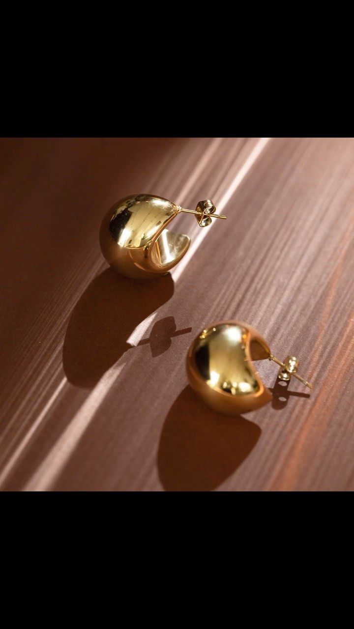 Boucles d'oreilles créoles rondes en or sur une surface texturée et brune, projetant des ombres.