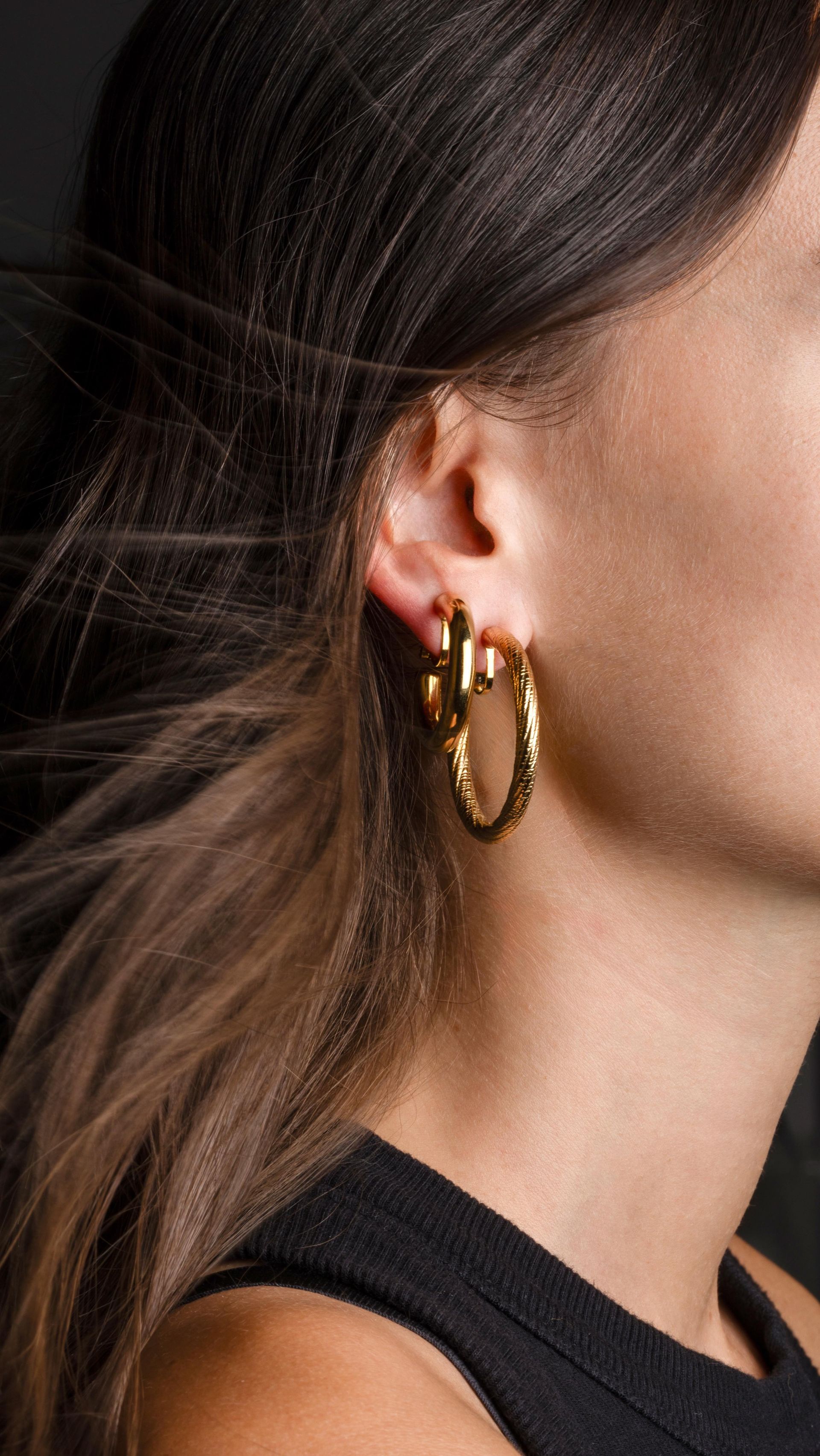 Femme portant des boucles d'oreilles créoles en or ; cheveux foncés, haut noir.