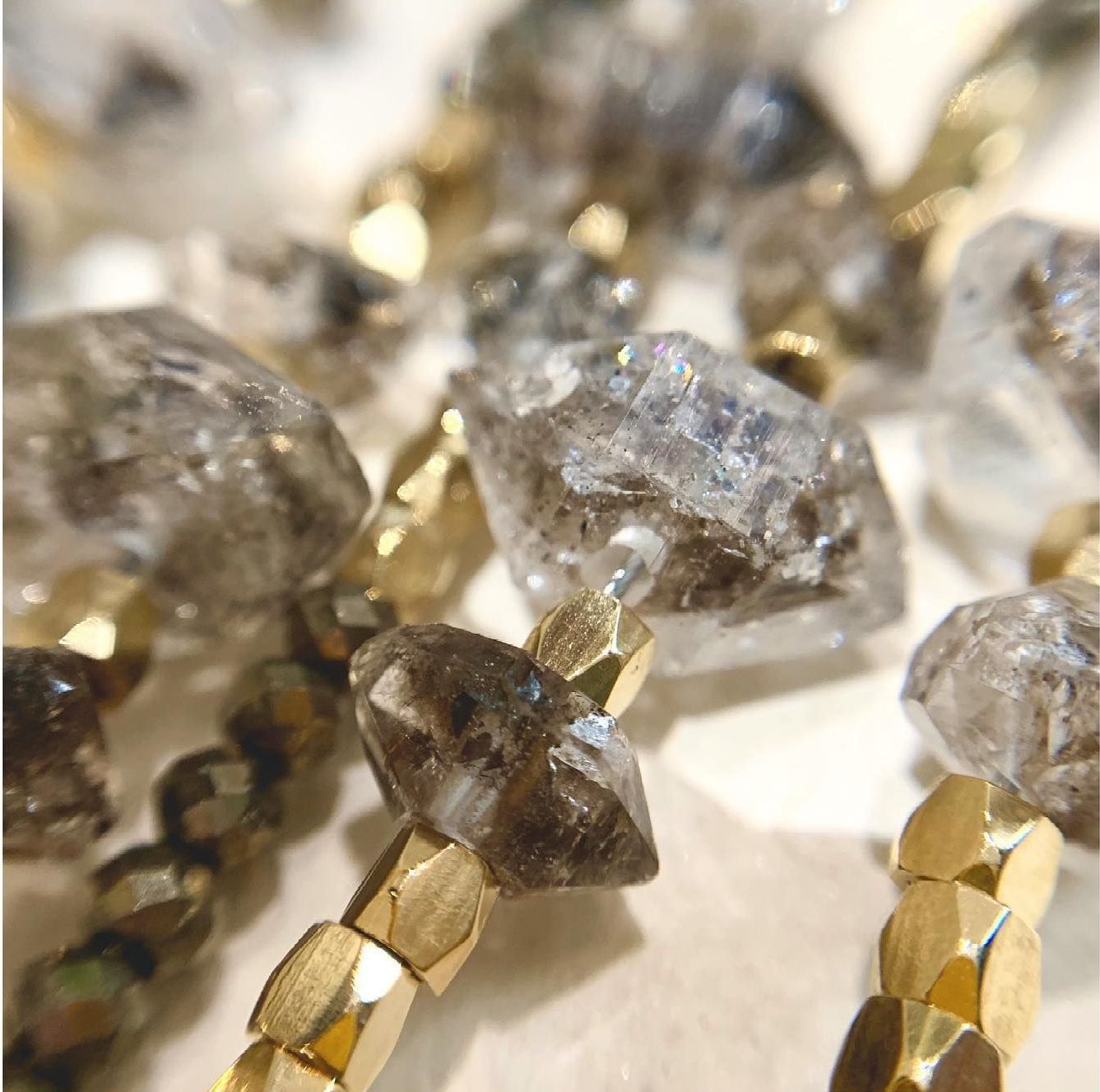 Gros plan d'un collier avec des cristaux gris taillés grossièrement et des perles hexagonales dorées.