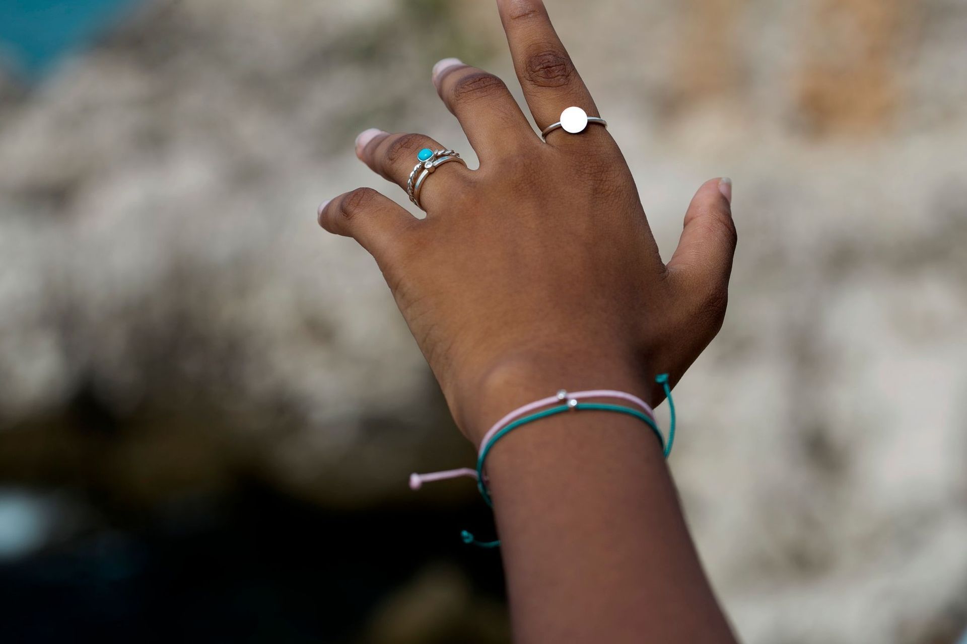 Main tendue avec des bagues et des bracelets en argent, sur fond extérieur flou.