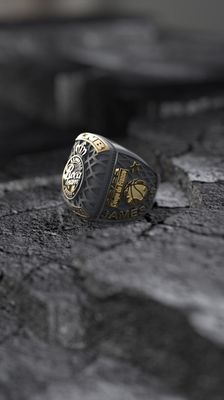 Bague en or et gris foncé sur une surface grise texturée ; présente des détails décoratifs et le chiffre « 70 ».