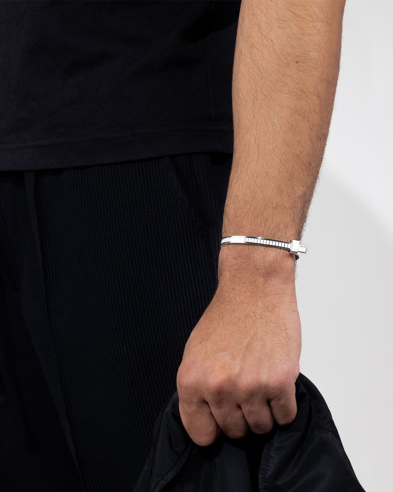 Personne portant un bracelet au poignet, tenant une veste noire.